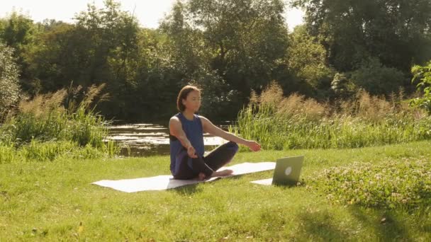 Dizüstü bilgisayarla yoga yapan bir kadın. Lotus pozisyonunda oturan ve meditasyon yapan bir kadın. — Stok video