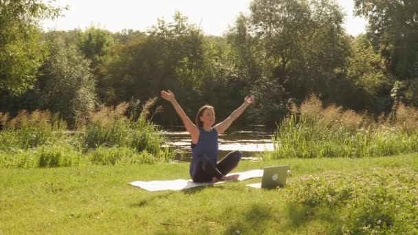 Tränar yoga utomhus. Kvinna som sitter i lotusställning och mediterar framför laptop — Stockvideo
