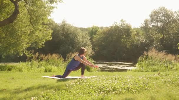 Mujer joven practicando yoga posan en el parque al amanecer. Meditación femenina en estera de yoga en el parque — Vídeo de stock