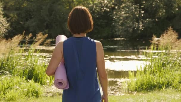 Mujer con tapete de fitness en las manos caminando en el parque de verano por la mañana — Vídeo de stock