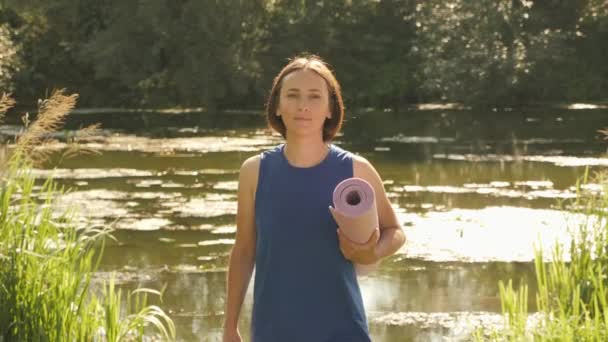 Retrato de mujer feliz y serena caminando en el parque de verano con colchoneta de fitness — Vídeo de stock