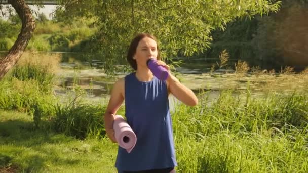 Acqua potabile femminile da bottiglia di plastica in natura. Fitness donna beve dalla bottiglia di sport — Video Stock