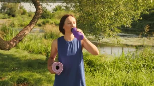 Mujer joven bebiendo agua de una botella de plástico. Chica bebe agua durante el día soleado — Vídeo de stock