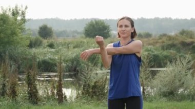 Eğitimden sonra kadın dışarıda esniyor. Egzersizden önce parkta esneme hareketleri yapan bir kadın.