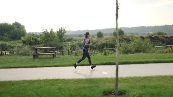 Una mujer corriendo por la mañana. Atlética joven hembra corriendo a lo largo del río en el muelle — Vídeos de Stock