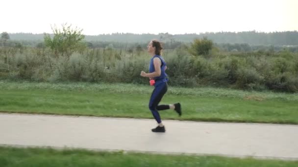 Біг на відкритому повітрі. Жінка біжить вранці вздовж спокійної річки в міському парку — стокове відео