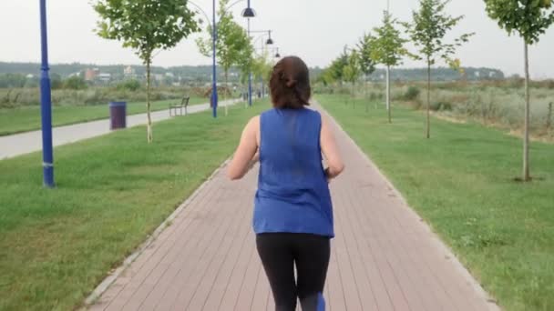 Running in city park. Back follow shot of young athletic woman jogging on promenade — Stock Video