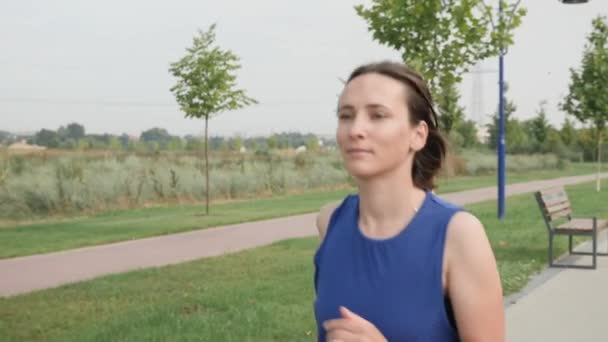 Corriendo. Motivada mujer confiada corriendo en el paseo marítimo en el parque por la mañana — Vídeos de Stock