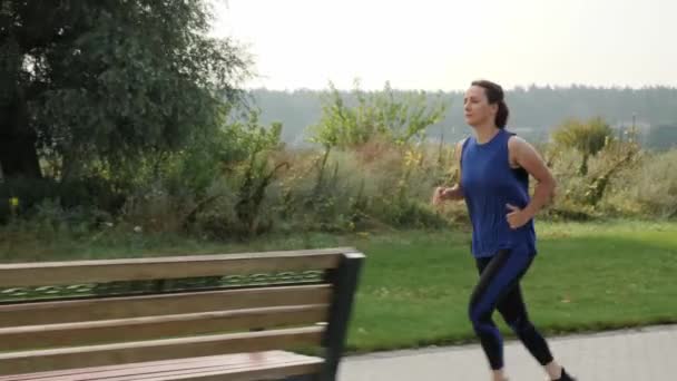Uma mulher activa a correr ao ar livre. Mulher determinada a atingir seus objetivos de aptidão esportiva — Vídeo de Stock