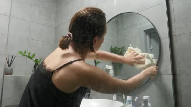 Жінка прибирає дзеркало вдома. Жіночий прибиральник, що витирає брудне дзеркало у ванній — стокове відео