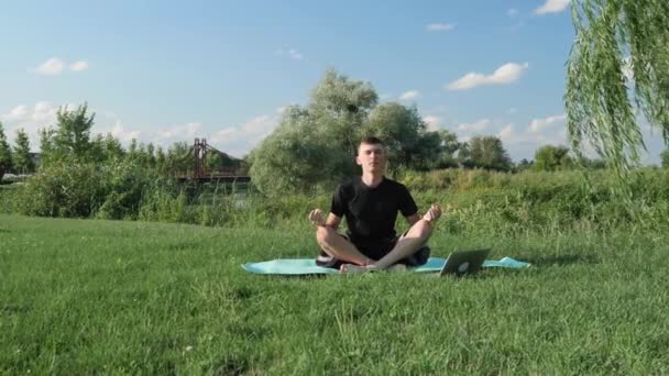 De mens beoefent yoga, mediteert in het park, poseert in lotus op een yogamat. Zen — Stockvideo