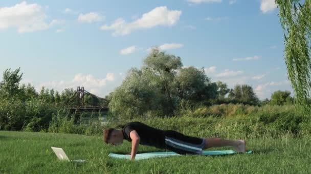 Muž dělá kliky na trávě v parku. Mužské cvičení fitness cvičení v dopoledních hodinách — Stock video