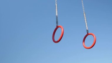 Açık havada mavi gökyüzüne el sallayan jimnastik ringi. Sallanan spor yüzükleri