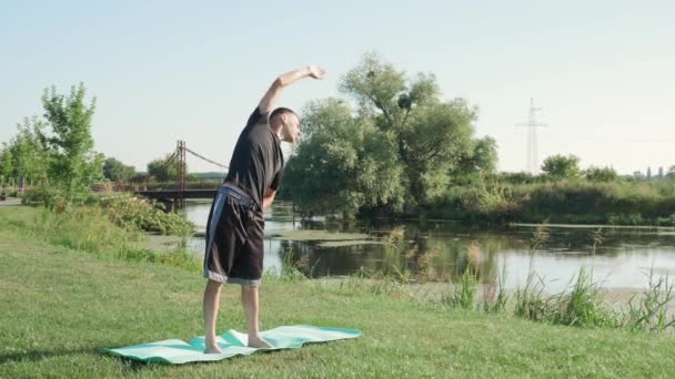 Hombre haciendo ejercicio en la alfombra de fitness en el parque de verano, estirando el cuerpo. Hombre haciendo ejercicio al aire libre — Vídeo de stock