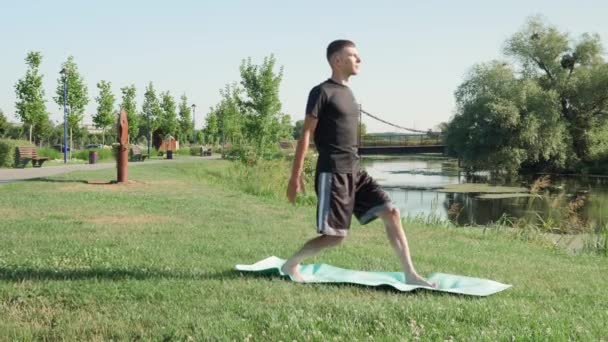 Seorang pria berlatih yoga pada fitness mat di taman di pagi hari. Latihan di luar ruangan — Stok Video