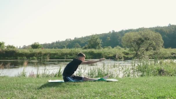 Fitness sport koncept. Muž protáhnout v letním parku podél řeky v dopoledních hodinách — Stock video