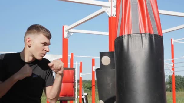 Jeune boxeur frappant un sac de boxe. Homme musculaire engagé dans la boxe avec sac de boxe en plein air — Video