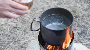 Doğada yemek pişirmek. Odun sobasında suyla tencereye tuz ekleyen bir kadın.