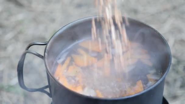 Adding grain into boiling water on fire. Cooking on nature. Preparing camping food on burning stove — Stock Video