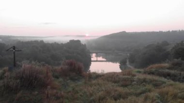 Gün doğumunda sisli bir sabah ormanı. Gün doğumunda ağaçlar ve nehirle destansı kır manzarası