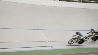 Bir grup profesyonel bisikletçi yüksek hızda bisiklet pistine biniyor. Sporcular velodromda antrenman yapıyor