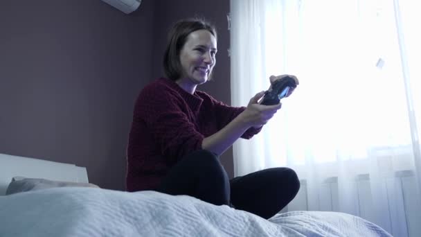 Молода збуджена дівчина сидить на дивані і грає у відеоігри за допомогою бездротового контролера — стокове відео