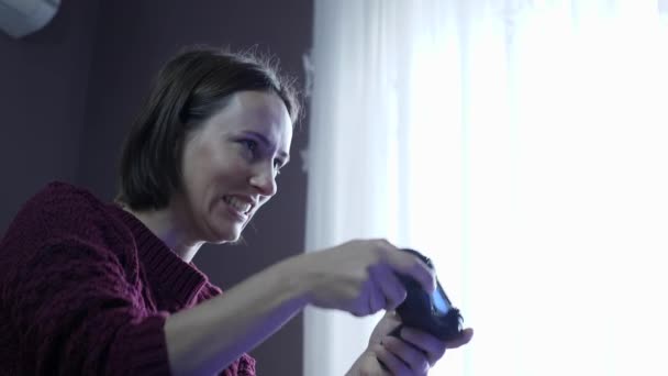 Радісна жінка грає в відеоігри перед телевізором, використовуючи бездротовий джойстик, насолоджуючись змаганнями відеоігри — стокове відео