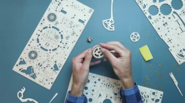 Erkek eller yapboz oyuncağının küçük tahta detaylarını tutuyor. Masada mekanik ahşap oyuncak