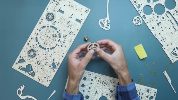 Człowiek montażu koła zamachowego szczegóły mechanicznej drewnianej zabawki na stole. Ręce trzymając małe drewniane szczegóły zabawki puzzle — Wideo stockowe