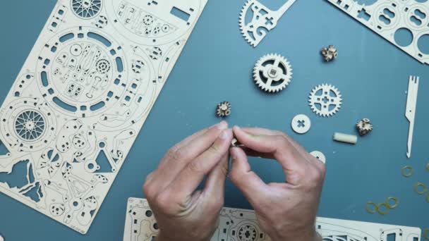 Man met kleine vliegwiel gear detail in de hand, het assembleren van mechanische houten puzzel speelgoed — Stockvideo