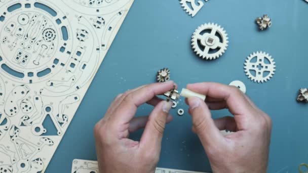 Manos masculinas usando cera para montar engranajes mecánicos de juguete de madera. Puzzle de juguete en la mesa — Vídeo de stock