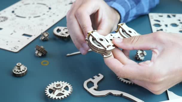 Montage van mechanisch houten speelgoed op tafel thuis. Man met mechanisch speelgoed in handen — Stockvideo