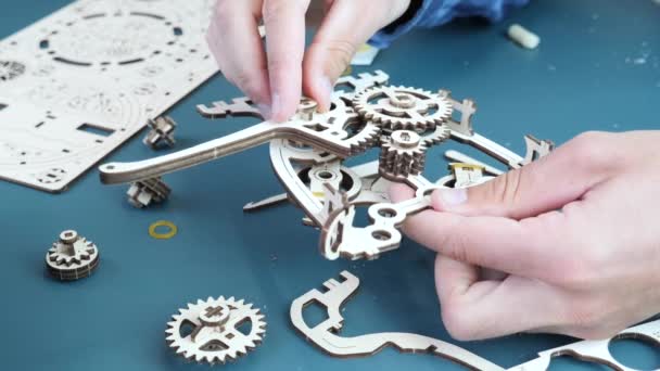 Człowiek montuje mechaniczne drewniane puzzle zabawki na stole. Ręce trzymające drewniane szczegóły zabawki — Wideo stockowe