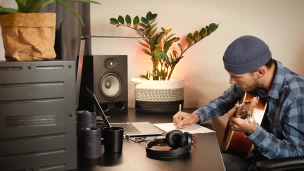 Músico componiendo música y escribiendo canciones. Hombre con guitarra tocando melodía y tomando notas en cuaderno — Vídeo de stock