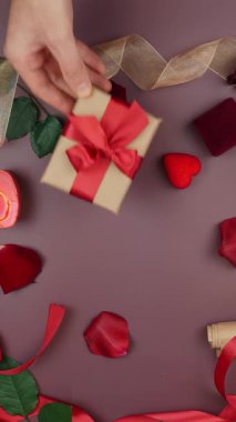 Erkek el, Sevgililer Günü 'nde gül ve mumlarla süslenmiş arka plandaki bayanlara kırmızı kurdeleli paket hediye paketi veriyor. Dikey video