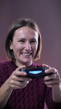 Gülümseyen ve gülen bir kadının evde kumandayla oyun oynaması portresi. Elinde kablosuz kumandası olan duygusal bir kadın. Dikey video