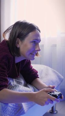 Heyecanlı gülümseyen genç kadın, kablosuz kumanda kullanarak konsolda oyun oynuyor. Gülümseyen neşeli kadın çevrimiçi video oyunları oynuyor. Dikey video