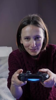 TV karşısında oturan ve joystickle video oyunu oynayan bir kadın, kapat. Kablosuz kumanda kullanan, evde oyun oynayan heyecanlı bir kadın. Dikey video