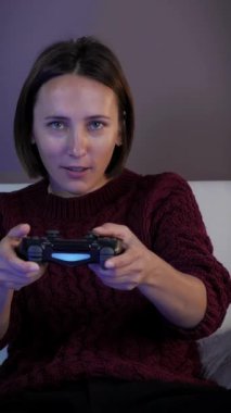 Kablosuz kontrolörle video oyunu oynayan mutlu bir kadın. Büyük televizyonun önünde oturan ve oyun oynamak için joystick kullanan bir kadın. Dikey video