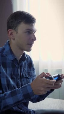 Video oyunları oynayan bir adam. Genç erkek evde kablosuz joystick ile video oyunu oynuyor. Dijital teknoloji. Dikey video