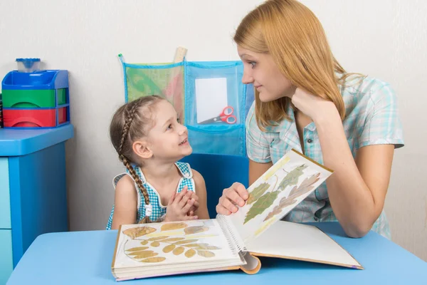 Five-year girl and mother looking at the herbarium of the leaves in the album looked at each other — Stock Photo, Image