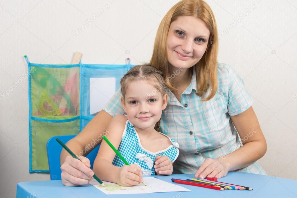 Five-year girl and young mother together paint a picture on a sheet of paper