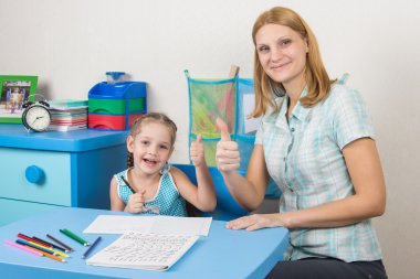 Akıl hocası ve beş yıllık kız sevinçle düzenli bir iş yaparak başparmak göstermek