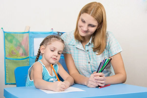 Das fünfjährige Kind zeichnet auf einem Blatt Papier, neben dem Lehrer hält es Bleistifte — Stockfoto