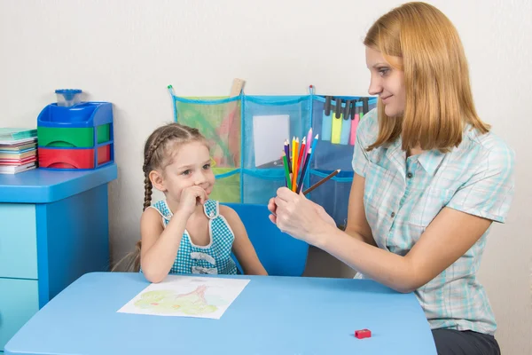 Five-year girl choose the right pencil from the teacher hands — Stock Photo, Image
