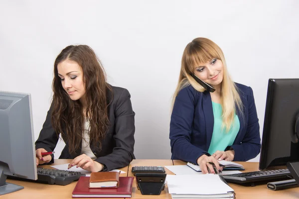 Unga flickor i kontoret, en fungerar i datorn, den andra på telefonen och titta på skärmen — Stockfoto