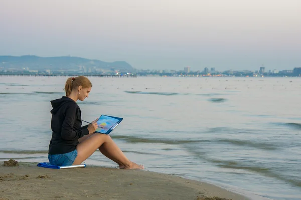 O jovem artista está sentado na praia e desenhando paisagem com pôr do sol — Fotografia de Stock