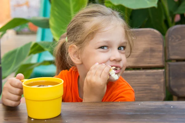 Hungry funny girl biting bun and drinking tea — Stock Photo, Image