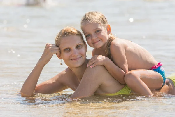 Girl sitting on the mother back, which lies in the sea — Stock Photo, Image