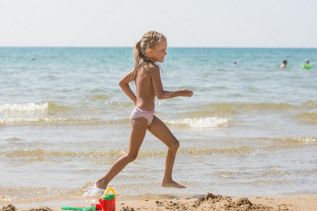 Five-year girl runs along the shore of the beach at the seaside